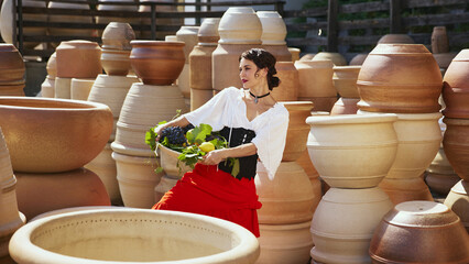 With confident pose, she holds her glass of wine aloft, proud smile on her lips against backdrop of carefully crafted pottery. Concept of end of summer, harvesting, travelling, natural beauty, culture