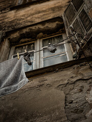 Weathered Facade Of An Old Building In Ventimiglia With Faded Shutters, Cracked Walls, And Laundry Hanging On A Clothesline Evoking Rustic Charm And Everyday Life In A Historic Italian Town.