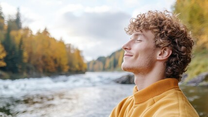 A young man enjoys tranquility by the riverside, surrounded by nature's beauty in autumn. A moment of peace and reflection.