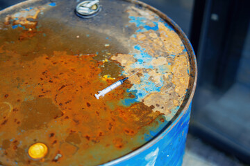 abandoned syringe rests on a rusted fuel barrel, symbolizing the juxtaposition of neglect and danger. This image evokes thoughts on waste, health, and environmental hazards