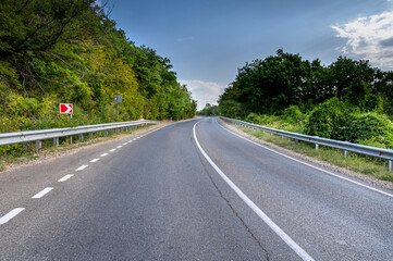 Road landscape forest and mountain. Empty long mountain road to the horizon on a sunny summer day with dramatic cloudy sky. Highway turn panoramic view.