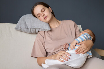 Sleepy woman parent with newborn kid experiencing discomfort and sleeping fitfully in living room...