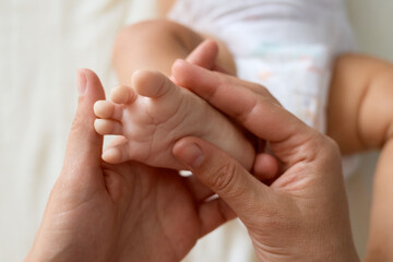 Unrecognizable mother doing massage for her healthy infant baby small Caucasian newborn laying on his back while his mommy performing massage for tiny feet