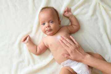 Unknown woman massaging belly of newborn baby on bed for stomach pain relief mother taking care of daughter or son health on white sheet at home