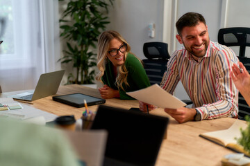 Fototapeta premium A group of colleagues having a cheerful discussion in a modern office setting. They are sitting around a wooden table with laptops, documents, and office supplies.
