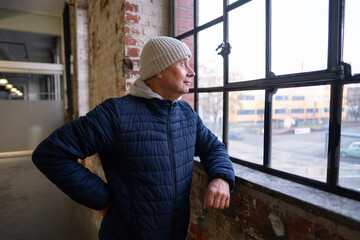 pensive elderly man, Charming lonely senior in quilted coat looks out window, lost in deep thought...