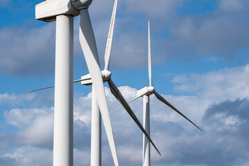 A detailed view of two wind turbines, focusing on their blades and structures against a partly cloudy sky, emphasizing modern technology in renewable energy production and environmental sustainabilit