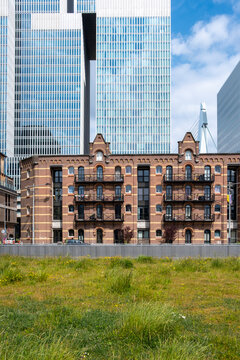 An old red-brick building stands between two sleek, modern towers, contrasting historical architecture with contemporary urban development and design in a vibrant city setting in Rotterdam