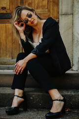 woman in a black suit and black high heels sits on a step