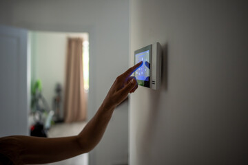 Closeup hand using smart home touch screen with connected appliances device on wall. Setting,...