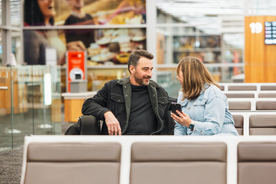 Man and woman watching phone together while waiting in airport departure lounge
