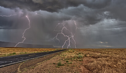 Lightning storm and grey storm clouds, over a straight road and the Vermilion Cliffs National Monument during the monsoon, Arizona, USA