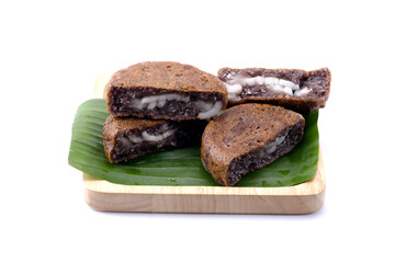 Black glutinous rice flour Thai coconut pancake on banana leaf in wooden tray isolated on white background closed up stack. Kanom Ba Bin in Thai.