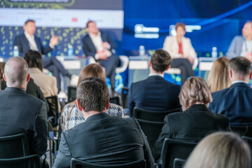Business professionals seated in an audience attending a corporate conference. Speakers,...
