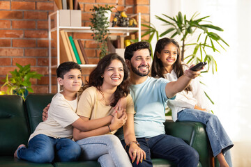 Happy Indian parents and kids sitting on a sofa, enjoying TV time together in the living room