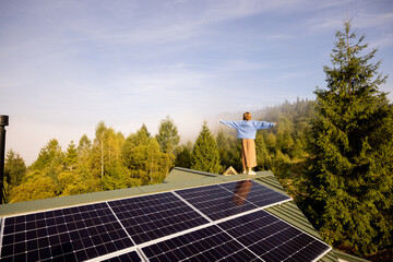 A woman stands on a solar-powered rooftop, arms outstretched, embracing the freedom and sustainability of off-grid living amidst a serene forested landscape © rh2010