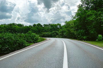 Fototapeta premium Road through the forest with clouds in the sky. Summer highway green concept. Asphalt road through the forest with clouds in a blue sky. Asphalt road through the forest nature with clouds and.