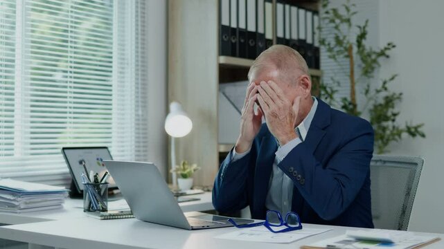 Businessman is seriously stressed and angry working on laptop and document paperwork and headache due to office syndrome on laptop and paperwork in the office.