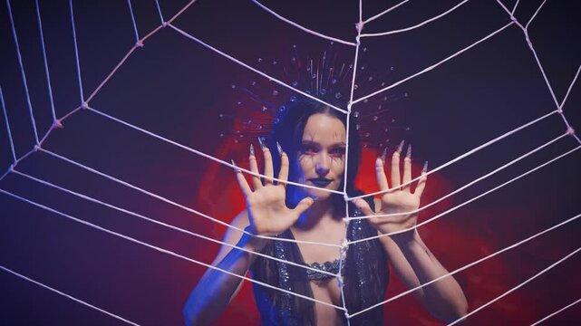 fantasy gothic vampire queen woman touches web with hand claws. creative holiday halloween style black lips makeup on beauty face Girl black widow spider nightmare crown on head. Night neon red light