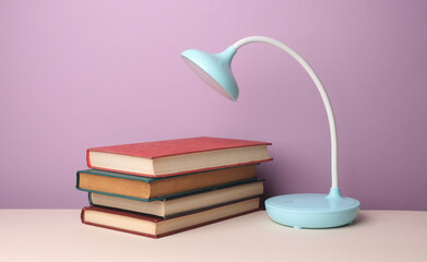 LED table lamp with stack of books on purple background. Energy saving