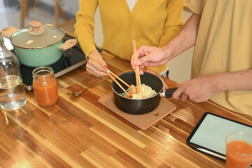 Close up shot of young couple preparing instant noodles in a small pot on a wooden countertop