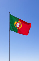 National flag of Portugal waving gracefully against a clear blue sky. The flag's vibrant red and green colors symbolize Portuguese pride and heritage, making it a powerful national symbol