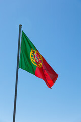 National flag of Portugal waving gracefully against a clear blue sky. The flag's vibrant red and green colors symbolize Portuguese pride and heritage, making it a powerful national symbol