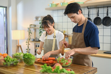 Loving young couple in aprons preparing a healthy salad together in their modern kitchen
