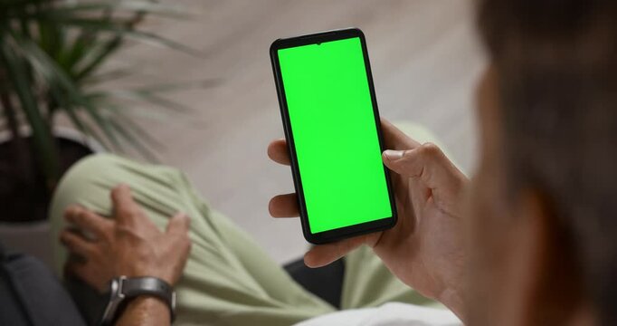 man sitting on couch and using mobile phone with chroma key green screen. swipe pictures, checking social media