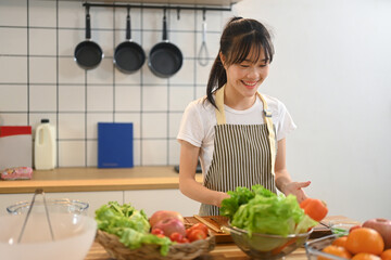 Smiling young asian woman wearing apron preparing a fresh and healthy salad in a kitchen