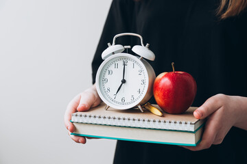 Teenage girl holding book, apple, and clock
