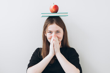 Teenage girl balancing books and apple, engaging in school activities