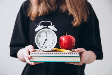 Teenage girl holding books, apple, and alarm clock, cropped view