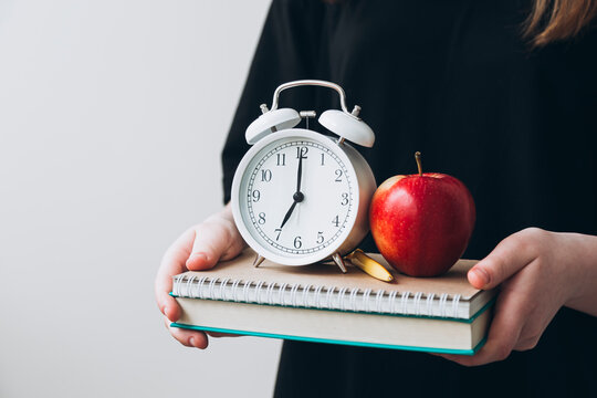 Teenage girl holding book, apple, and clock