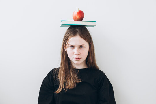 Teenage girl with apple and books, staring at camera