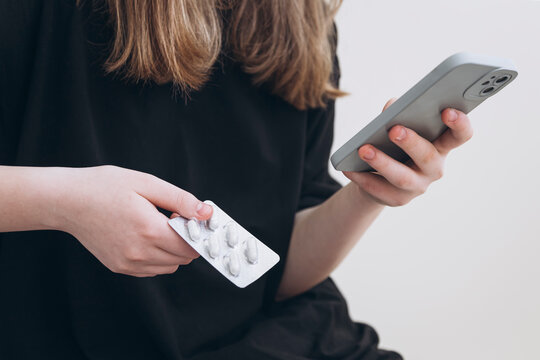 Teenage girl examines pills while holding smartphone