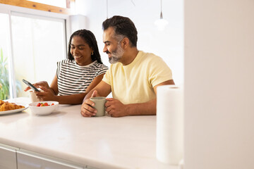 Multiracial couple enjoying breakfast and using smartphone