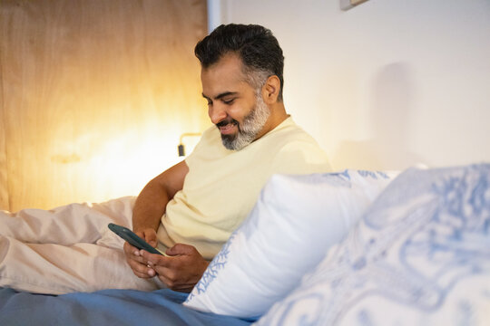 Indian Man relaxing in bed with smartphone at home