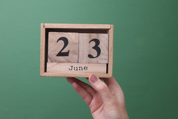 Hand holding wooden block calendar with the date June 23 on green background