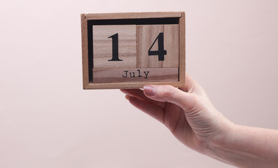 Female Hand holding wooden block calendar with the date July 14 on beige background