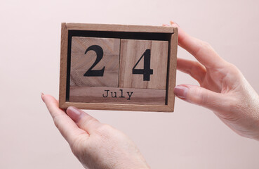 Female Hand holding wooden block calendar with the date July 24 on beige background