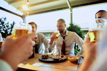 Sunny day meeting in outdoor bar, group of professionals drinking lager beer after long day, engaging in lively conversation. Concept of business, meeting, fun, celebration, leisure time, Oktoberfest