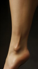 A close-up view captures the graceful curve of a delicate ankle, showcasing its smooth, unblemished skin against a dark background