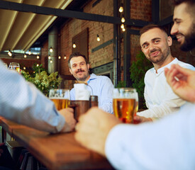 Positive men, business people, colleagues meeting in outdoor bar, talking, drinking beer and having good relaxing time after work. Concept of business, meeting, celebration, leisure time, Oktoberfest