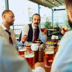 Positive men, business people, colleagues meeting in outdoor bar, talking, drinking beer and having good relaxing time after work. Concept of business, meeting, celebration, leisure time, Oktoberfest