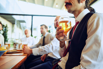 Colleagues, businessmen relaxing at the bar with beers, balancing work with bit of fun. Celebrating well-coordinated teamwork and success. Concept of business, meeting, fun, Oktoberfest