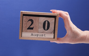 Female Hand holding wooden block calendar with the date August 20 on a blue background