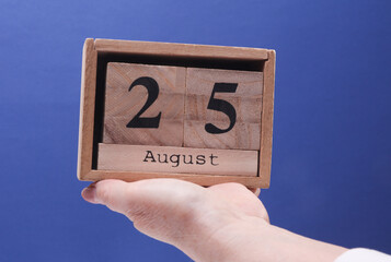 Female Hand holding wooden block calendar with the date August 25 on a blue background