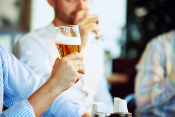 Focus on male hand holding glass of lager beer with thick foam. Business People meeting at local bar for relaxation after hard working week. Concept of business, meeting, leisure time, Oktoberfest