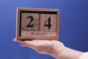Female Hand holding wooden block calendar with the date August 24 on a blue background
